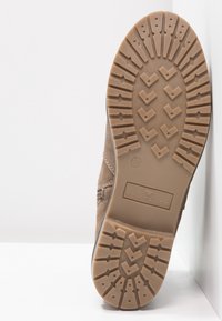 Bottine en suède marron avec une semelle en caoutchouc texturée, présentant un motif de bande de roulement pour l'adhérence, et marquée du logo "TOM TAILOR" sur le talon. Taille 37.