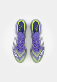 Cizme de fotbal violet și verzi, cu un superior texturat, design elegant și accente albe. Șireturile și brandul sunt vizibile pe limbă.