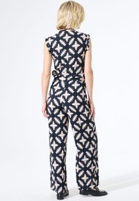 Zwart en crèmekleurig jumpsuit met een mouwloos ontwerp, een relaxte pasvorm en wijde pijpen. Kenmerkt zich door hoekige vormen in de textuur van de stof.