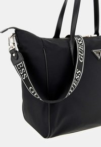 Zwarte totebag van nylon, met dubbele leren handvatten en een logo-geprinte schouderband. Inclusief een driehoekige logoplaat op de voorkant.