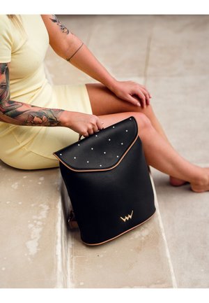 Černý kožený batoh s zaobleným klopou, tečkovanými akcenty a zlatým logem. Obsahuje světle hnědý lem a nastavitelné popruhy pro všestrannost.