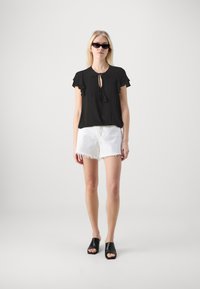 Svart kortermet bluse med volanger og knyttet hals. Kombinert med hvite, slitte denimshorts og svarte åpne mules.