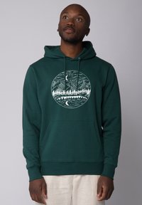 Groene hoodie met een voorzak, met een witte grafiek van bergen en bomen in een cirkelontwerp. Zacht materiaal.