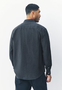 Camicia grigia scuro con bottoni e motivo a quadri texturizzato; presenta maniche lunghe e colletto standard.