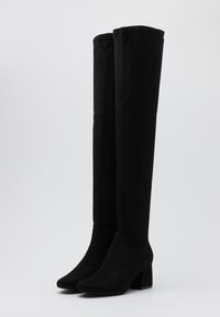 Botas negras hasta la rodilla hechas de suave ante, con un diseño elegante, tacón cuadrado y puntera puntiaguda. Textura lisa sin patrones visibles.