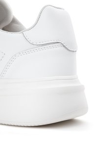 Białe sneakersy z gładką skórzaną cholewką, okrągłym obcasem i przeszyciami wzdłuż szwów. Podeszwa jest gruba i teksturowana.