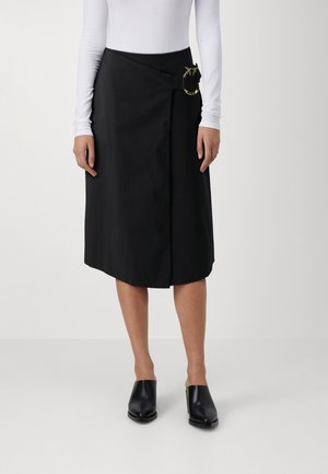 Fustă neagră cu legătură laterală și accesoriu auriu. Fabricată dintr-un material neted, cu o lungime până la genunchi. Purtați cu mules negre cu toc.