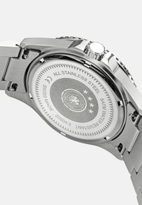 Rückseite einer Edelstahl-Armbanduhr mit gravierten Details, kreisförmigem Design, Wasserdichtigkeitsbewertung und dem Hinweis "Schweizer Präzision".