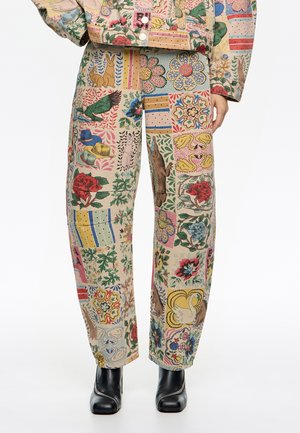 Pantalones de tela multicolor con un patchwork de patrones florales y animales. Diseño holgado con piernas rectas, complementados con botas negras.