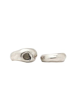 Anello in argento con un design ondulato, caratterizzato da un ritaglio ovale su un lato e una superficie liscia e lucidata. In generale, un aspetto moderno e scultoreo.
