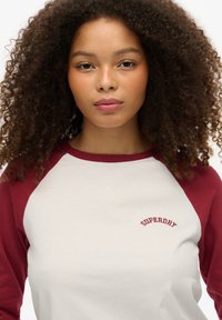 Raglan-sleeve T-shirt in off-white and maroon, met een logo in rode draad op de linkerborst, van katoen en met een ruime pasvorm.