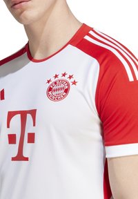 Valkoinen ja punainen jalkapallopaita, jossa on röpelöinen pinta. Paidassa on FC Bayern Münchenin logo ja punainen Telekomin sponsorilogo edessä.