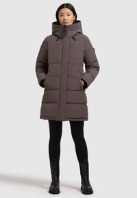 Grey puffer coat with a high collar and hood, zip closure, front pockets, and a quilted design. Worn over black leggings and boots.