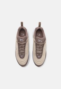 Baskets de sport beiges et marron avec un tissu texturé, bout rond, semelle intermédiaire blanche et surpiqûres décoratives. Logo Nike sur la languette et sur le côté.