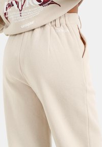 Beige sweatpants met een gladde textuur, elastische tailleband, zijzakken en discrete branding aan de voorkant in het wit. Casual ontwerp.