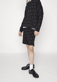 Black hoodie and matching shorts, both with yellow smiley face patterns. Worn with white socks and black shoes. Casual cotton material.