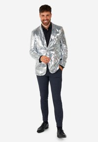 Silver sequined blazer with black shirt, dark trousers, and black shoes. Features shiny material and tailored fit. Complete stylish look.