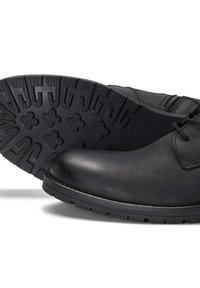 Close-up van zwarte leren schoenen met een gestructureerde rubberen zool, die het elegante ontwerp en de details op het bovenste deel tonen.