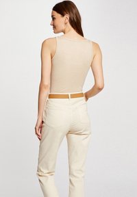 Beige sleeveless top with a smooth, shiny texture, paired with light beige high-waisted jeans. A brown belt accents the outfit.