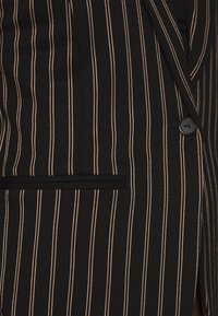 Black blazer with thin beige stripes, featuring a single black button, a chest pocket, and a textured fabric finish.