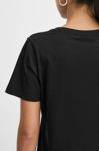 T-shirt di cotone nera con maniche corte, scollatura rotonda e una texture liscia e uniforme. La vista posteriore mostra un design semplice senza motivi o accenti.