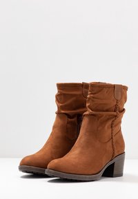 Stivali in suede marrone a metà polpaccio con tacchi bassi a torre, zip interna e dettagli intrecciati sul lato esterno.