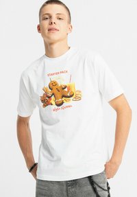 Biały bawełniany t-shirt z nadrukiem przedstawiającym piernikowego ludzika, przekąski oraz czerwony napis "STARTER PACK", z okrągłym dekoltem.