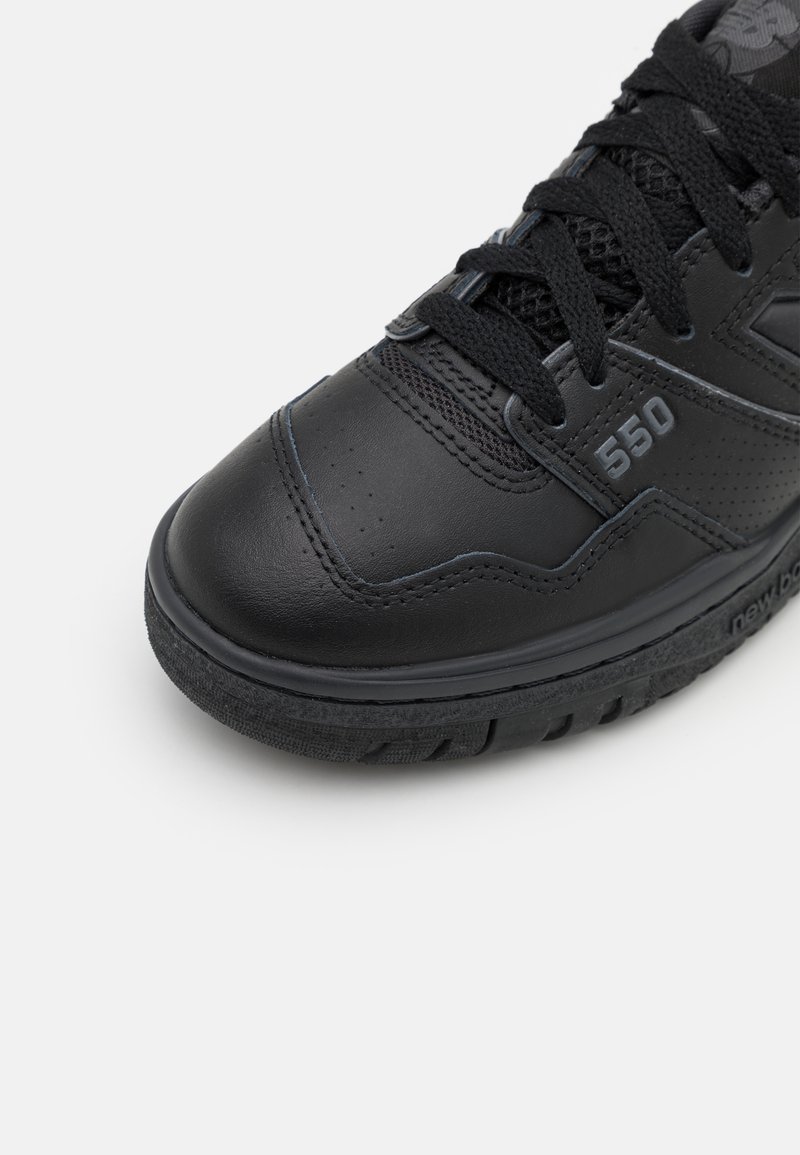 Chaussure de sport noire avec une tige en cuir lisse, des accents en maille, une semelle texturée et un logo visible avec le numéro de modèle 550.