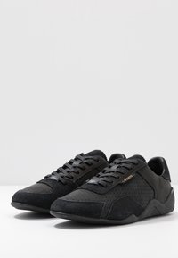 Baskets noires mêlant cuir lisse et daim perforé. Elles présentent un design à lacets et des accents texturés sur les côtés.