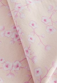 Țesătură din bumbac de culoare roz pal, cu modele florale delicate în alb și roz, având o textură subtilă. Două straturi pliate, evidențiind detaliile designului.