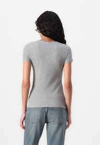 Tricou gri cu dungi, cu mâneci scurte și decolteu rotund, purtat cu blugi din denim de culoare albastru deschis, cu talie înaltă, văzut din spate.