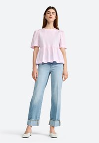 Lyserød peplum top med korte puffærmer, parret med høj talje lyseblå jeans med foldede manchetter og hvide flade sko.