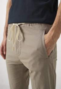 Lichtbeige broek met een elastische tailleband en trekkoord. Voorzien van zijzakken en een gladde, textuurstof.