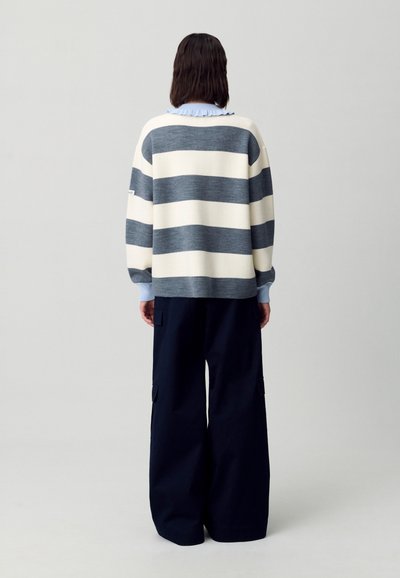 Maglione a righe in crema e blu navy, vestibilità rilassata con spalle scese, abbinato a pantaloni a gamba larga blu navy con dettagli sulle tasche.
