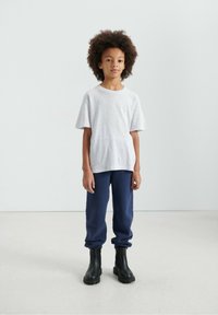 Pelēka īsroku t-krekls kopā ar tumši ziliem treniņbiksēm un melniem potīšu zābakiem. Apģērbs ir brīva piegriezuma un vienkārša dizaina.