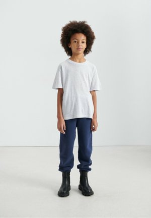 Maglietta grigia a maniche corte abbinata a pantaloni della tuta blu navy e stivali alla caviglia neri. L'outfit presenta una vestibilità comoda e un design semplice.