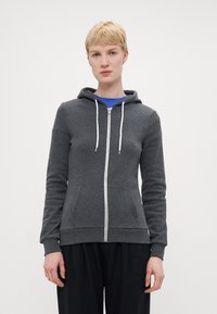 Grå zip-opp hettegenser laget av mykt stoff, med hette, hvite snorer og frontlommer. Fitted med ribbede mansjetter og nederkant.