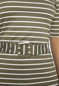 Zielono-biała pasiasta bluzka o dopasowanym kroju z pasującym paskiem z tego samego materiału. Pasek ma prostokątną klamrę i kilka otworów.