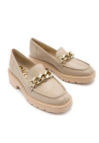 Beżowe skórzane mokasyny z masywną podeszwą, z złotym łańcuchem na przodzie i teksturowaną powierzchnią. Okrągły design noska.