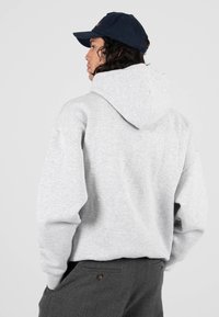 Šedá mikina s kapucí z texturované látky, volný střih a širokými rukávy. Kombinována s tmavě šedými kalhotami, doplněna námořnickou čepicí.