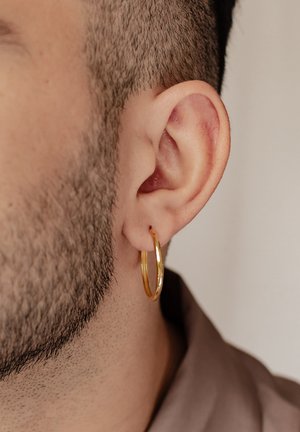 Gold hoop earring hanging from the lobe, featuring a smooth, shiny texture. Short, dark hair and close-cropped beard visible.