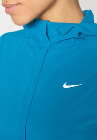 Nike kaputanje u vibrantnoj plavoj boji, s visokom kragnom, zatvaranjem na patentni zatvarač i malim bijelim logom na prednjoj strani. Glatka, lagana tkanina.