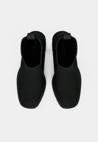 Crne lagane cipele bez vezivanja s glatkom gumiranom površinom, zaobljenim vrhom, teksturiranim rubom i ravnim potplatom. Ime marke vidljivo unutra.