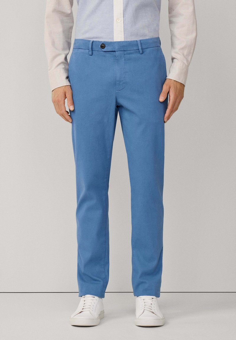 Chinos azzurri chiari in cotone, con taglio dritto, passanti per cintura, tasche frontali e chiusura con un solo bottone. Abbinati a sneakers bianche.