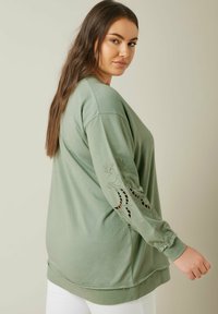 Sudadera de manga larga verde menta con acentos bordados en las mangas, corte relajado, textura suave y puños acanalados.