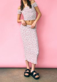 White floral crop top with off-shoulder sleeves, paired with a matching midi skirt. Worn with black platform sandals. Pink background.