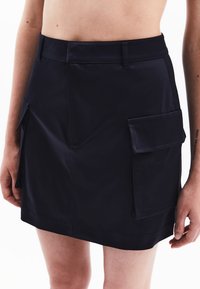 Donkerblauwe mini jurk gemaakt van een gladde stof, met een hoge tailleband, opgestikte zakken aan de zijkanten en een rechte zoom.