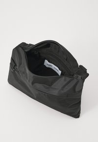 Svart nylonveske med glidelås i hovedrommet og en frontlomme. Har glatt tekstur og minimalistisk design.