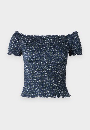 Marineblauwe off-the-shoulder top van smock stof, met een bloemenpatroon van kleine witte en groene bloemen. Zachte textuur, korte mouwen.