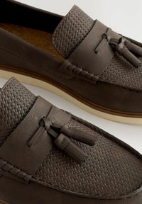 Mocassins en cuir marron avec une texture tissée sur le dessus, des détails à franges et une semelle claire.